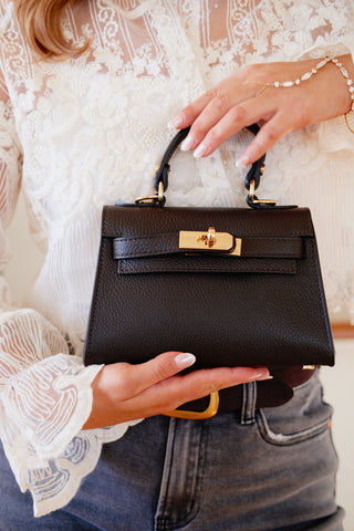 Person holding a black handbag with gold accents and diamond hand chain. Birkin look-alike with lace top